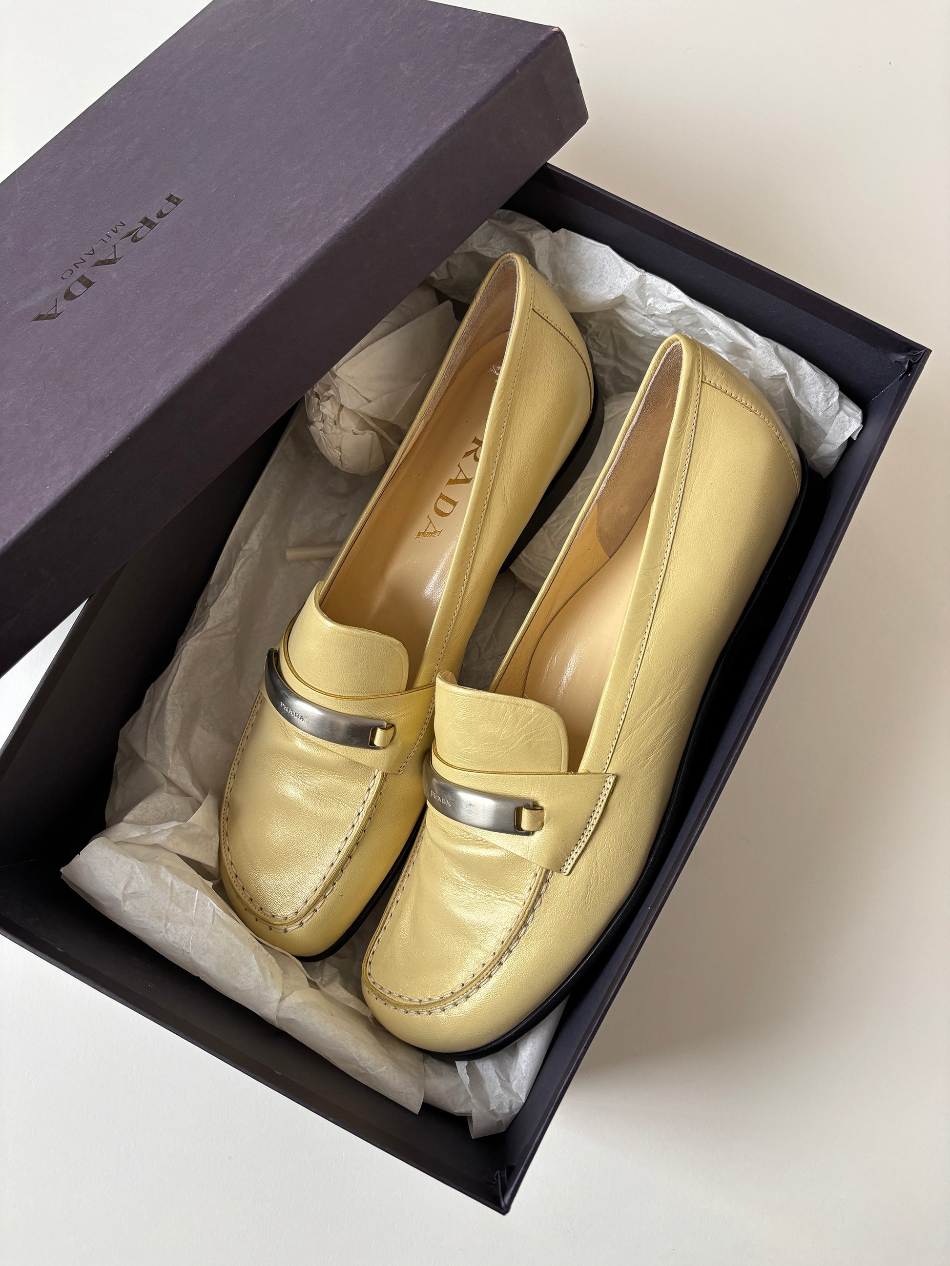 Vintage Prada 1990s pearly butter yellow loafer with metal logo detail.